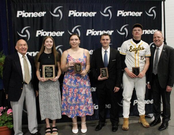 Six people posing with plaques in front of a Pioneer backdrop; three students hold awards, flanked by two men in suits.