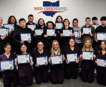 Group of students posing with certificates in front of a Mid-Ohio Educational Service Center banner.