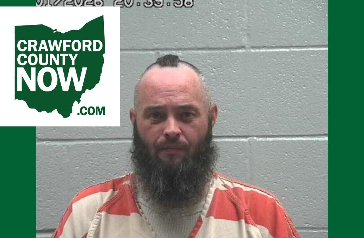 Mugshot of a bearded man in an orange prison jumpsuit against a gray cinder-block wall, with a Crawford County Now logo overlay on the left.