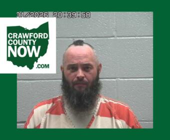 Mugshot of a bearded man in an orange prison jumpsuit against a gray cinder-block wall, with a Crawford County Now logo overlay on the left.