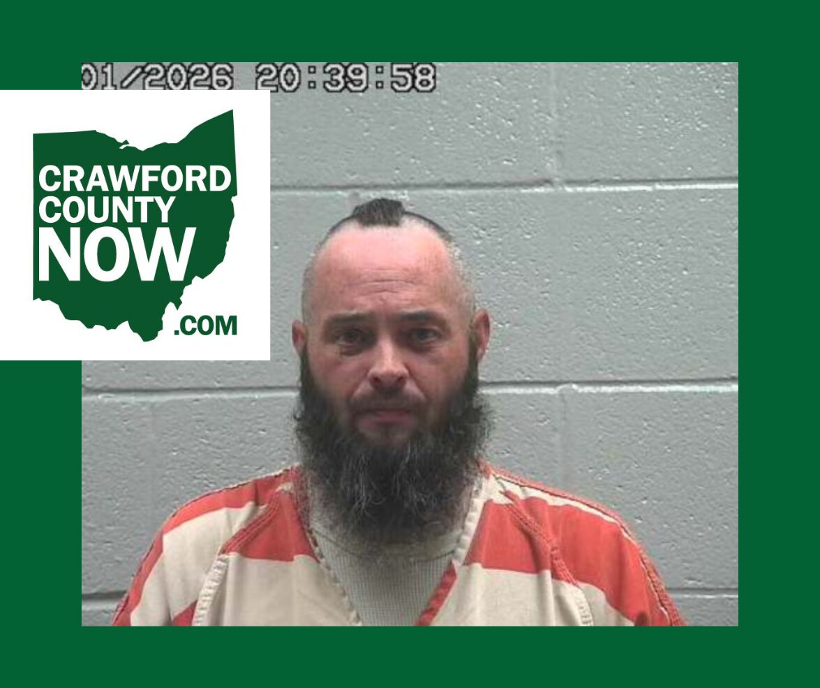 Mugshot of a bearded man in an orange prison jumpsuit against a gray cinder-block wall, with a Crawford County Now logo overlay on the left.
