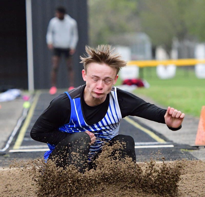Male athlete landing in a sand pit during a long jump, sand spraying as he hits the track.