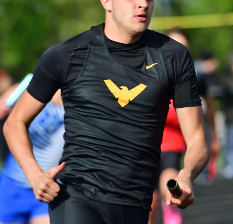 Male track athlete in black uniform running with a baton during a relay race on an outdoor track distance scene