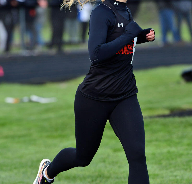 Young female athlete sprinting on a track in black athletic wear with a ponytail flowing behind her.
