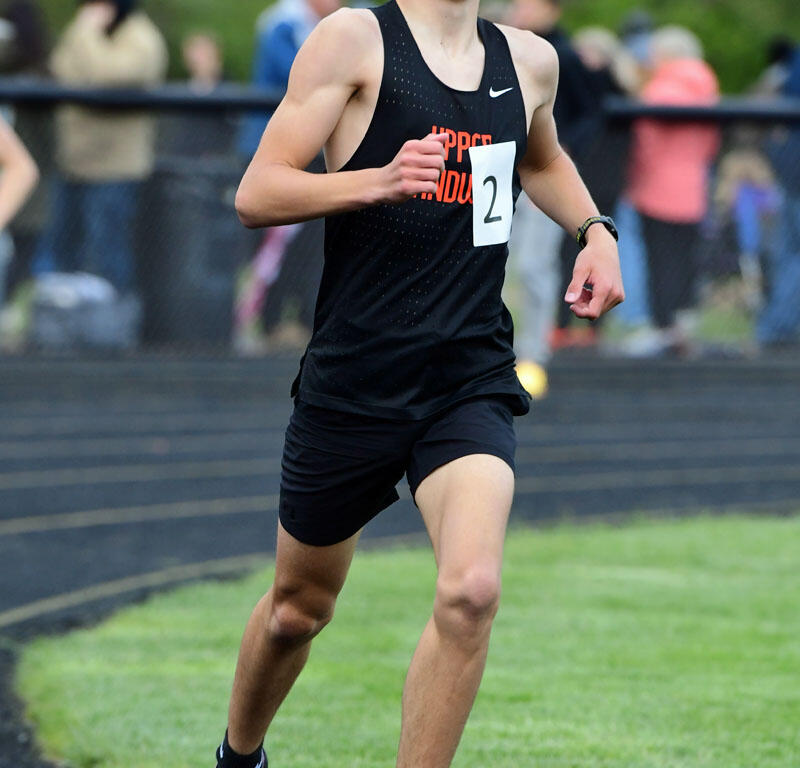 Young male runner in a black singlet and shorts sprints on the track wearing bib 2, with spectators in the background.