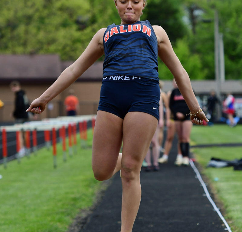 Female athlete in a blue Galion uniform mid‑air during a long jump on an outdoor track runway