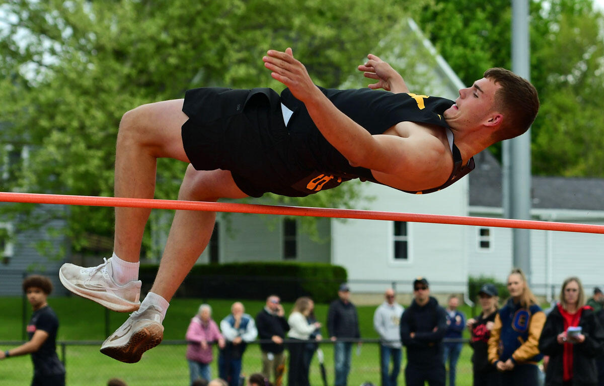 Male high jumper clears an orange bar in a track and field event, spectators watching in the background.