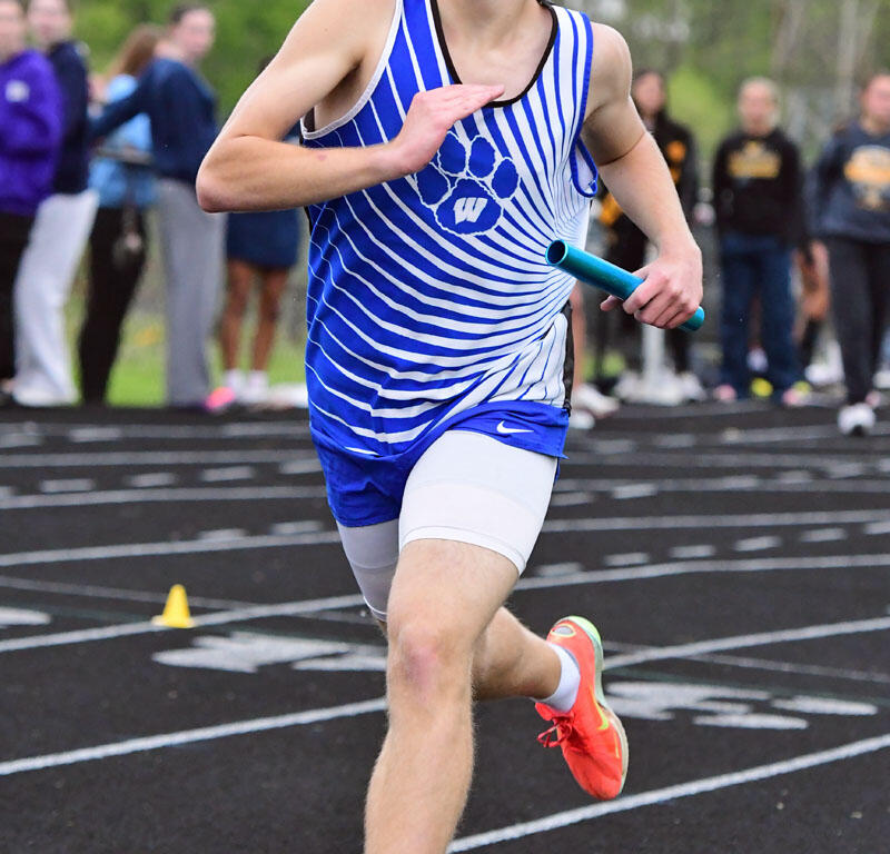 Male baton runner in a blue and white striped uniform sprints on a track, wearing mirrored sunglasses.