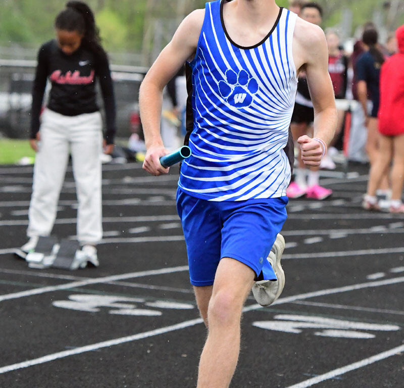 Male sprinter in a blue and white striped singlet runs on a track holding a turquoise relay baton during a race.