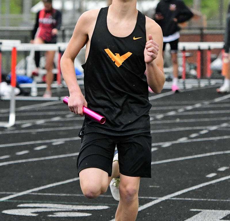 Young male sprinter in a black uniform runs on a track, holding a pink relay baton.