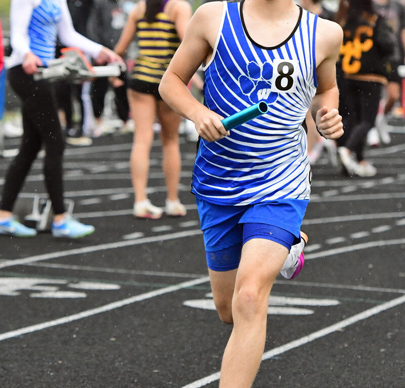 Relay race runner on an outdoor track, holding a blue baton, wearing a blue striped singlet with number 8.