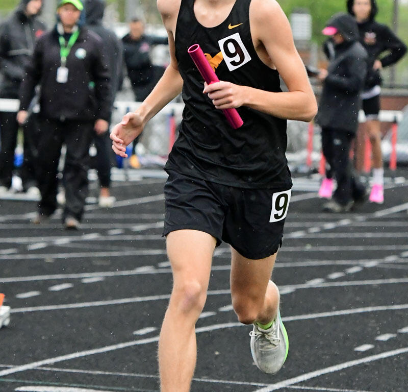 Relays runner in black uniform with bib 9, sprinting on track while holding a pink baton, wearing sunglasses.