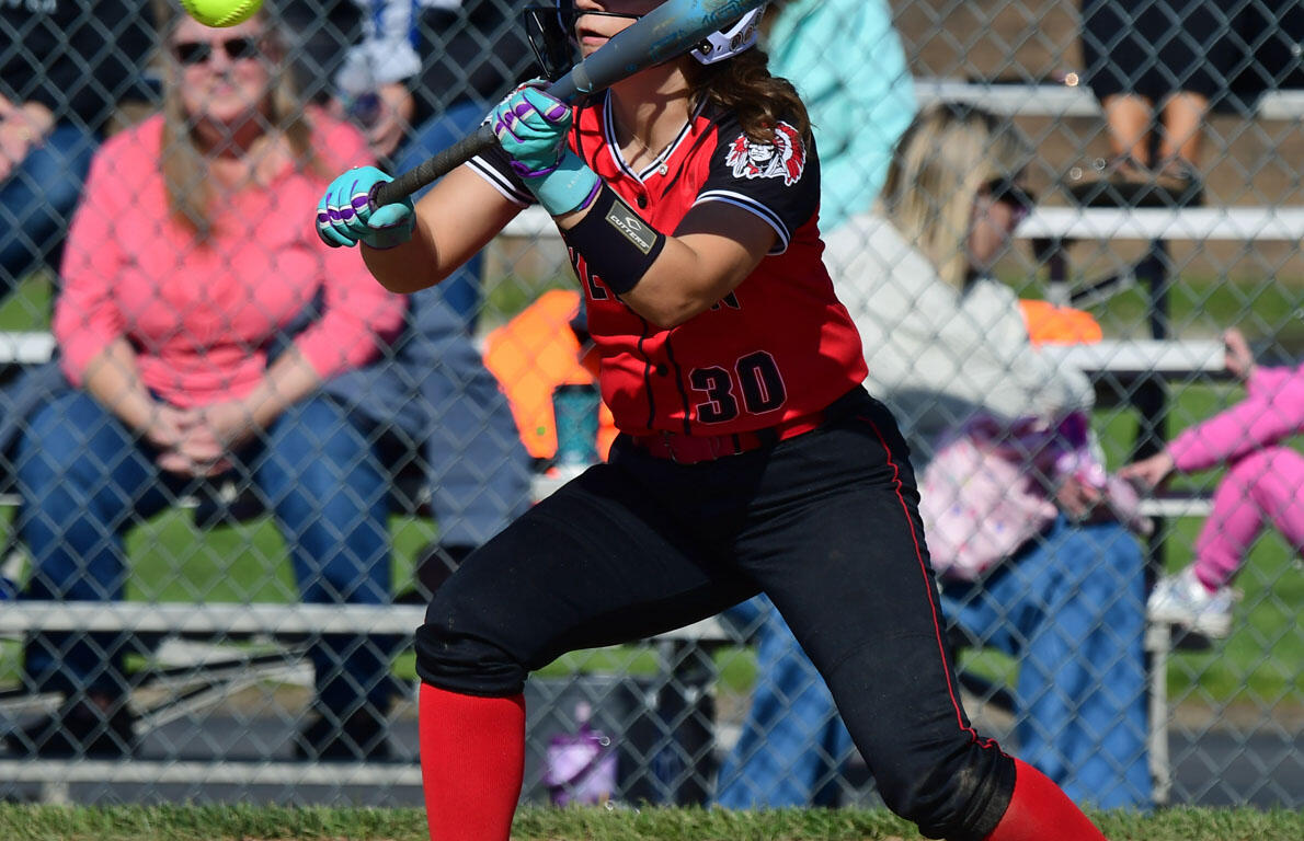 Female softball batter in red uniform with number 30, swinging at a pitch during a game behind a chain-link fence.