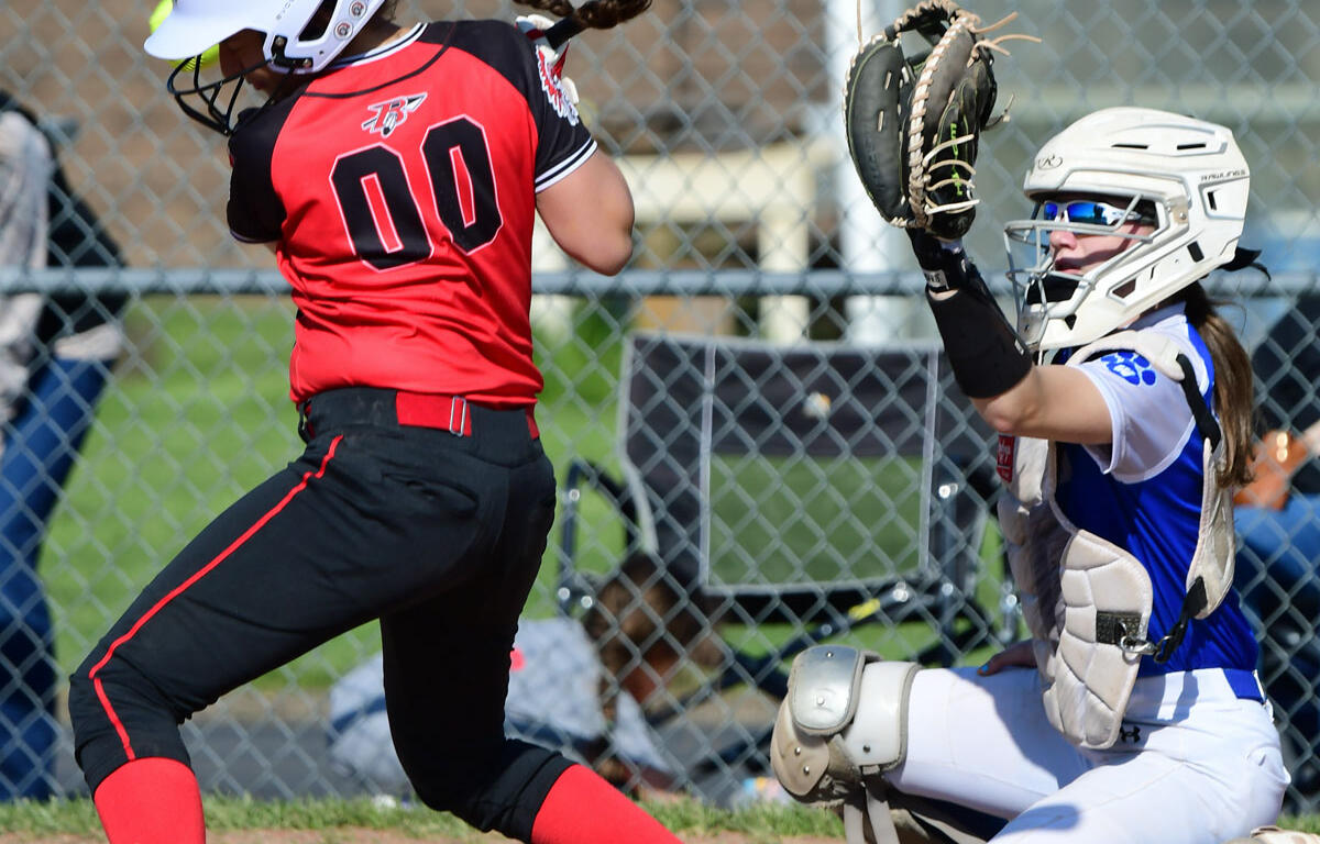 Softball batter in red and black with number 00 swings at a pitch as the blue-and-white-clad catcher crouches behind home plate with glove raised.