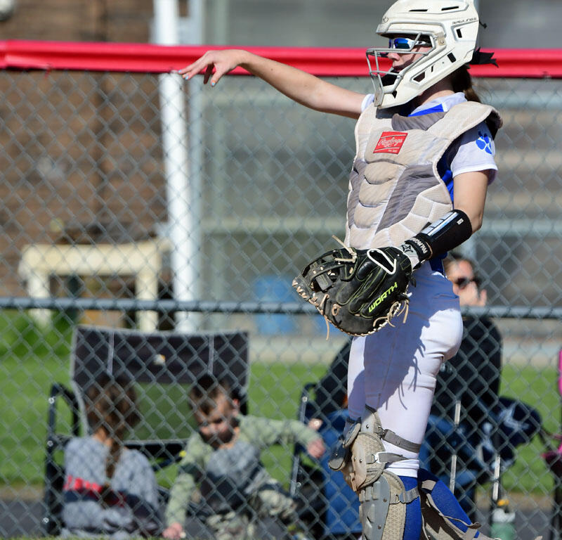Softball catcher in helmet and protective gear throwing a ball midair from the field.