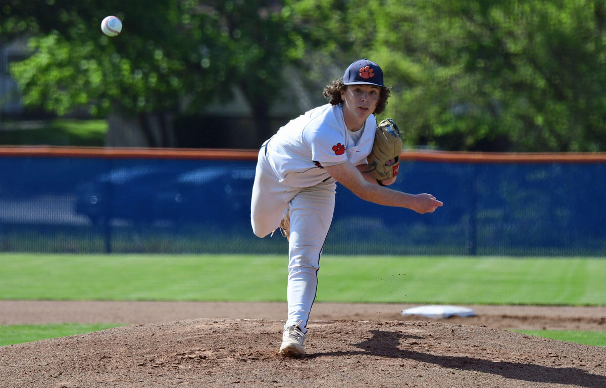 Baseball pitcher in a white uniform on the mound throwing a pitch, with the ball in midair nearby.