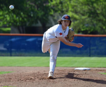Baseball pitcher in a white uniform on the mound throwing a pitch, with the ball in midair nearby.