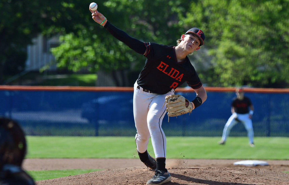 Baseball pitcher in black ELIDA jersey delivering a pitch on the mound with glove ready to catch, during a game.