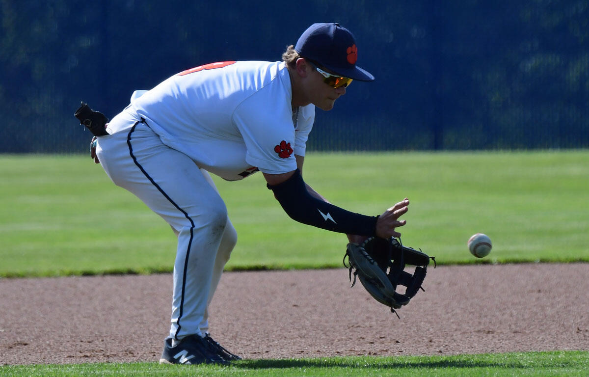 Baseball infielder in a white uniform crouches with glove ready to field a ground ball on the infield dirt.