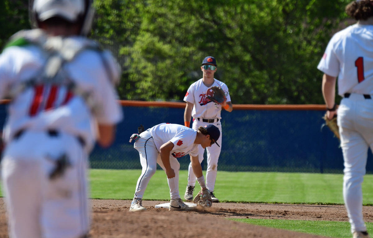Baseball game scene with a fielder bending to touch second base as a teammate watches nearby on the sunny field.
