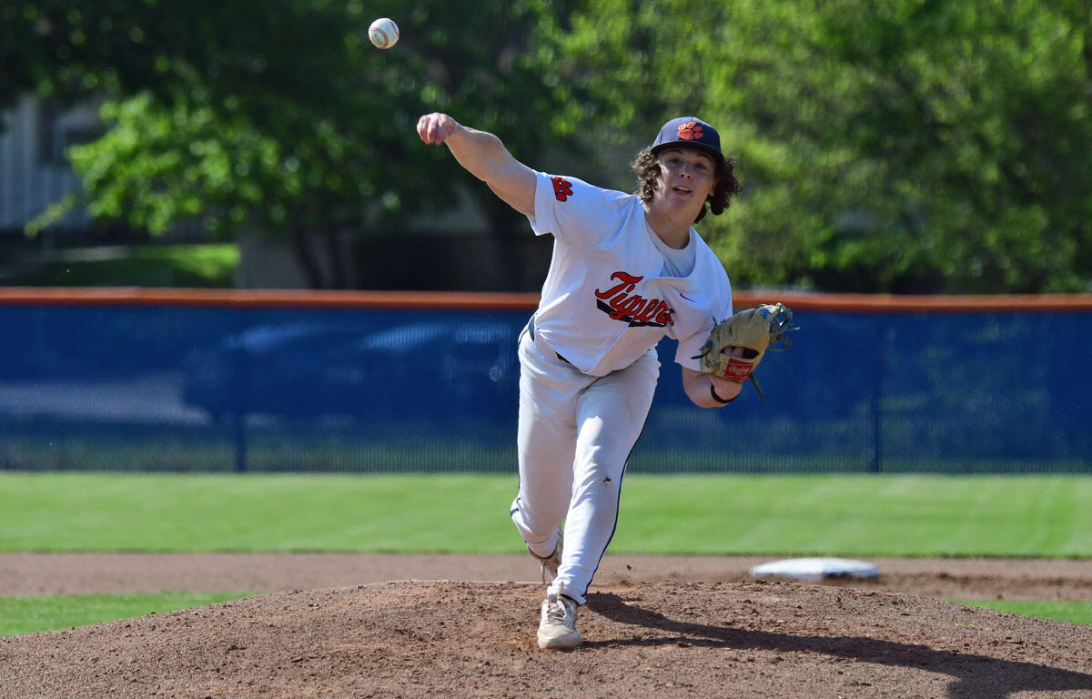 Baseball pitcher in a white Tigers jersey delivers a pitch from the mound, ball mid-flight toward home plate.