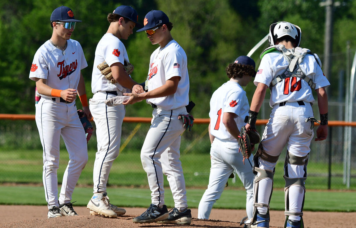 Group of baseball players in white uniforms with orange paw logos, shaking hands on the infield dirt under a sunny sky.