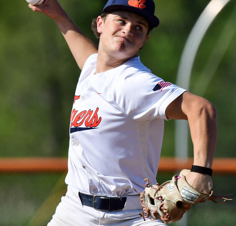 Baseball pitcher in a white uniform throws a ball mid-pitch on a sunny field.