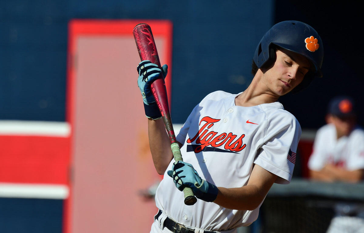 Baseball player in Tigers uniform swings a pink bat during a game, wearing a navy helmet with an orange paw logo.