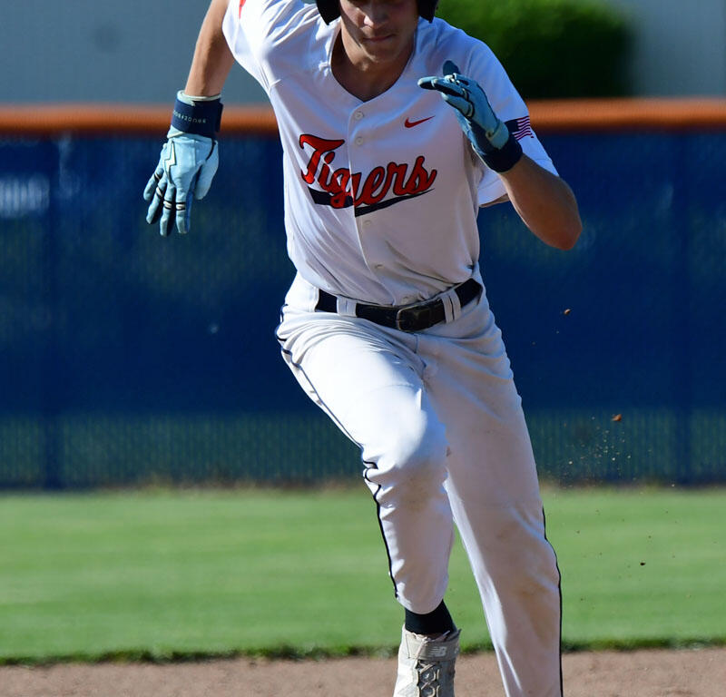 Baseball player in a white Tigers uniform runs on the infield, wearing a blue helmet with an orange paw logo.