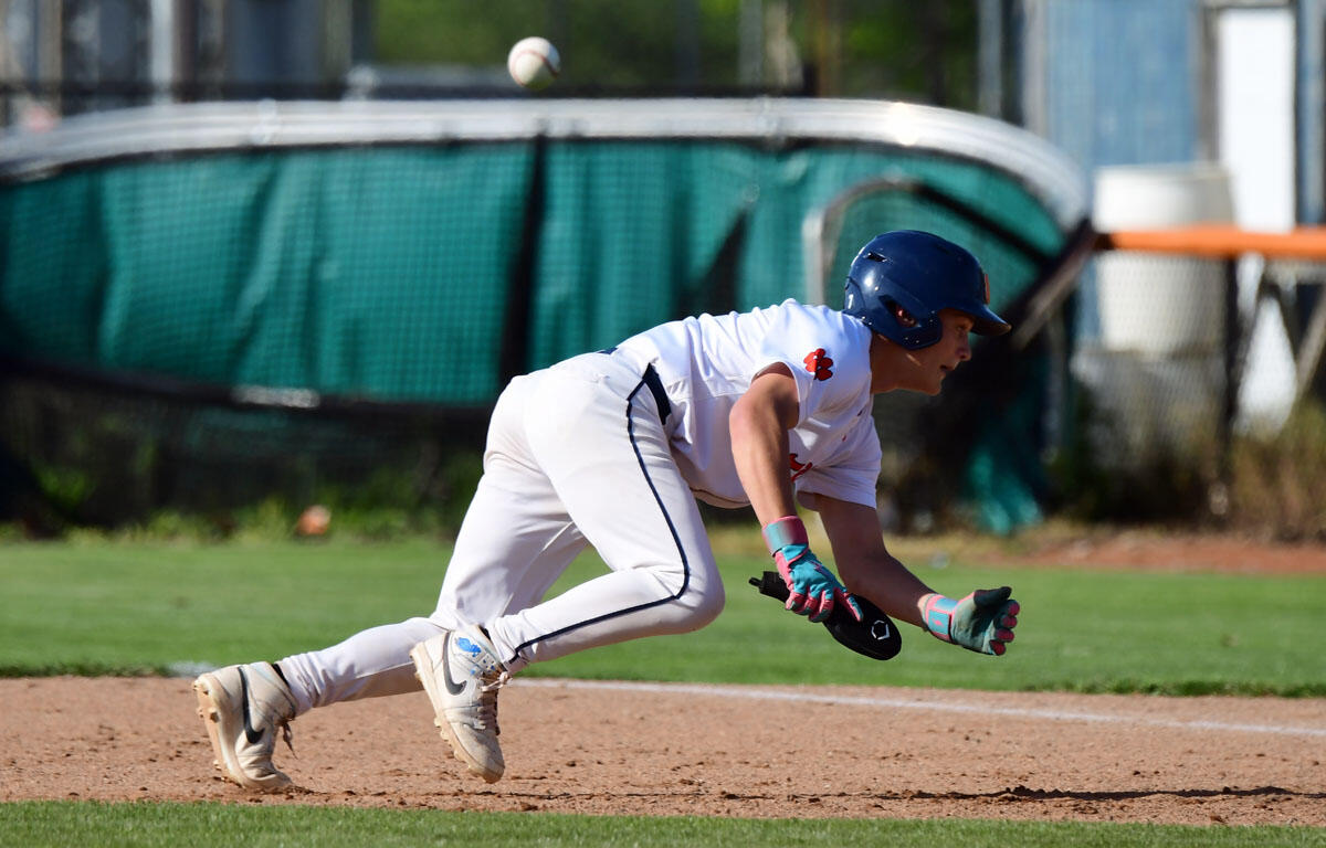 Baseball player in white uniform and blue helmet slides on dirt, glove extended to reach a ball in midair.