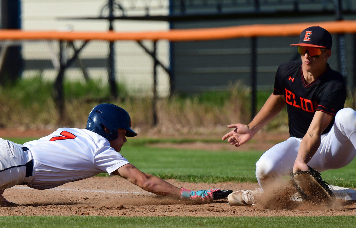 Baseball play action: a white-uniformed runner slides headfirst toward a base as a fielder in black reaches with a glove; dirt kicks up around them.