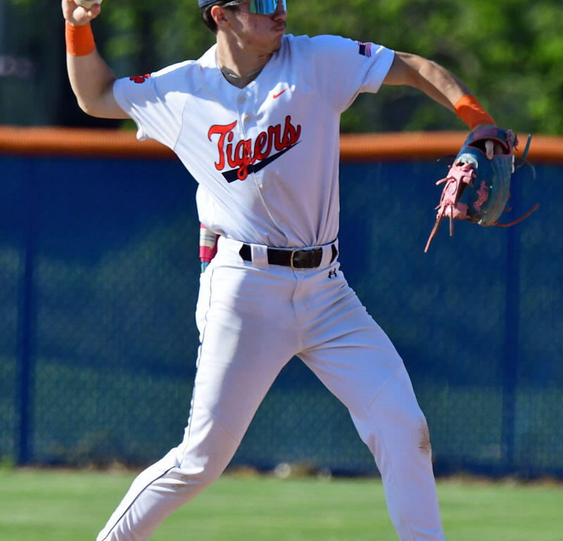 Baseball player in a Tigers uniform preparing to throw, standing on a base with glove on his left hand and ball in his right hand.