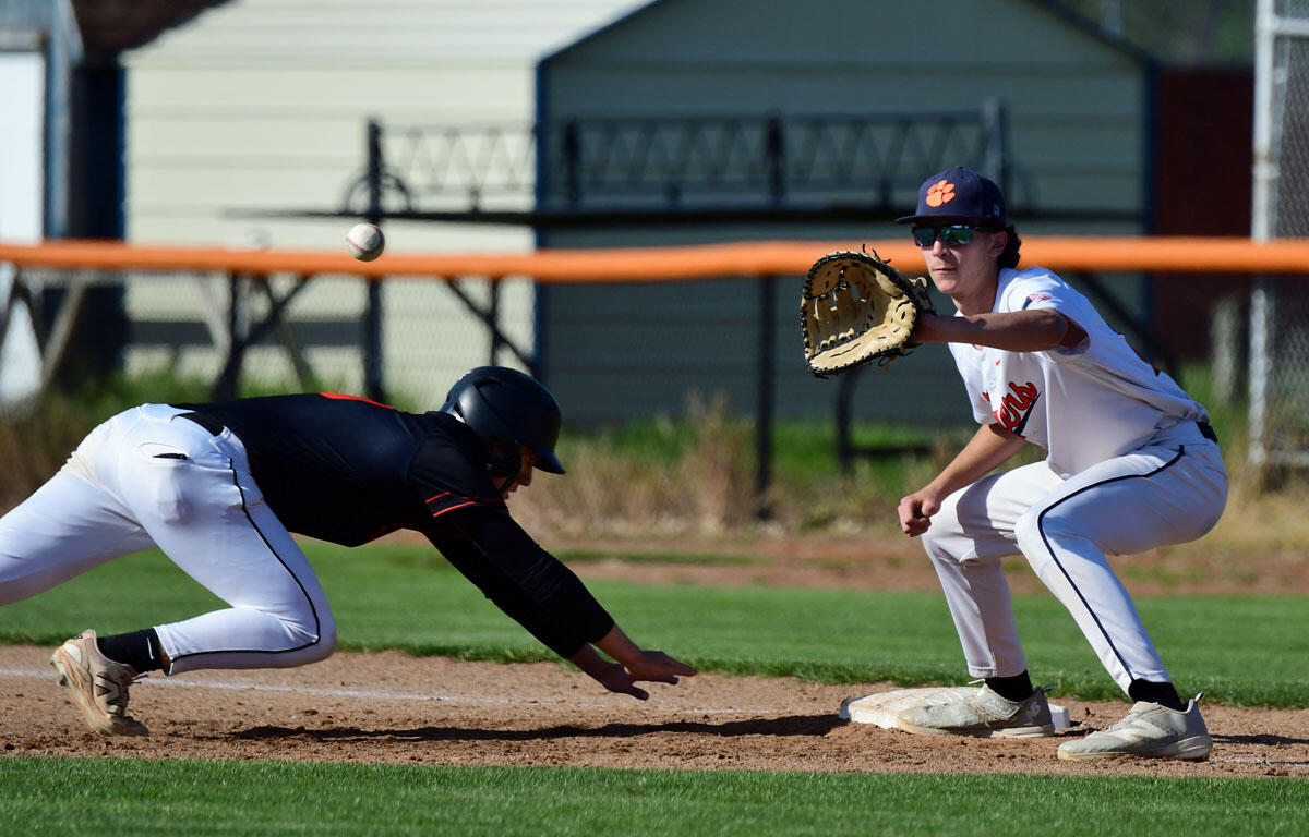 Baseball: white-uniform fielder lunges with glove as a baserunner in black slides toward the base; ball in midair.