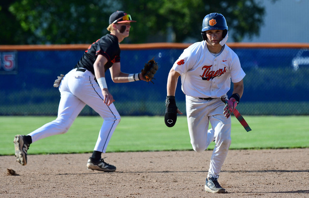 Baseball action: a Tigers baserunner in white sprints toward first base with a pink bat, as a fielder in black closes in behind him.