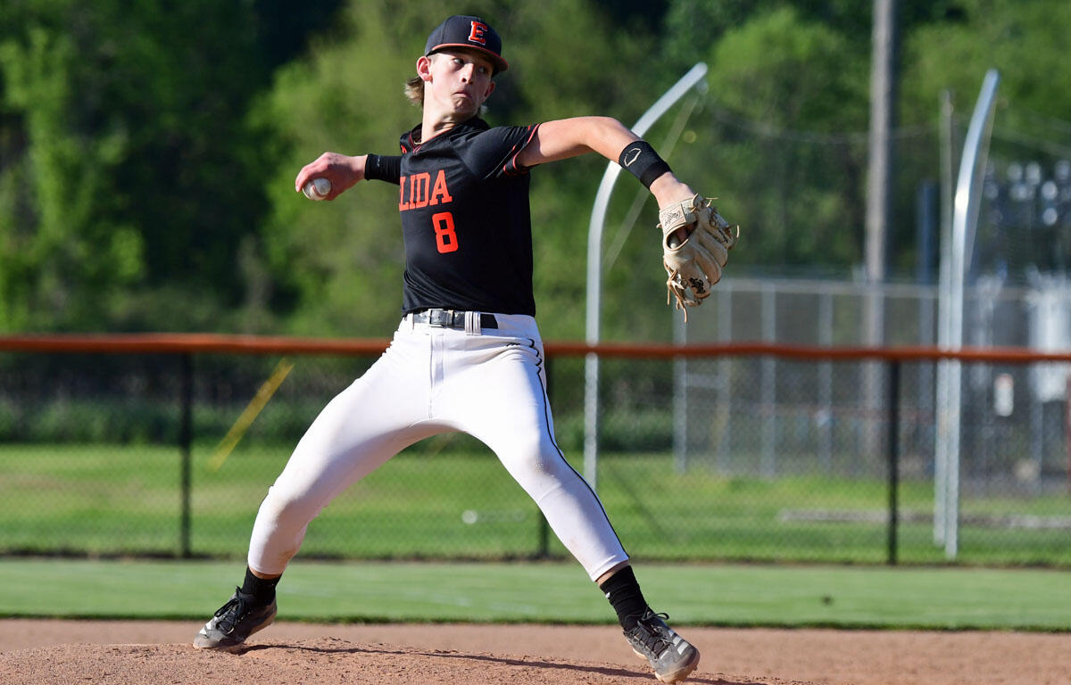 Baseball pitcher in black jersey with orange lettering and number 8 delivering a pitch on the mound outdoors.