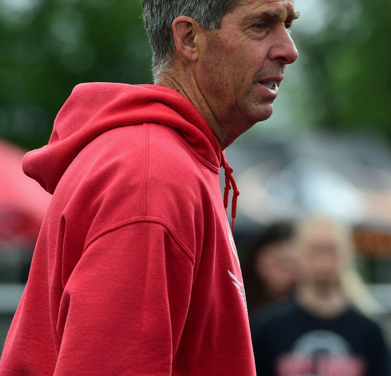 Side profile of a middle-aged man wearing a red hoodie outdoors, looking to the right with a blurred green background.