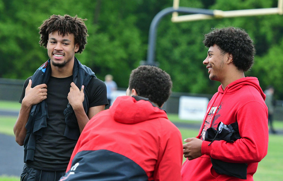 Three young men on a track field, smiling and talking outdoors after a workout.