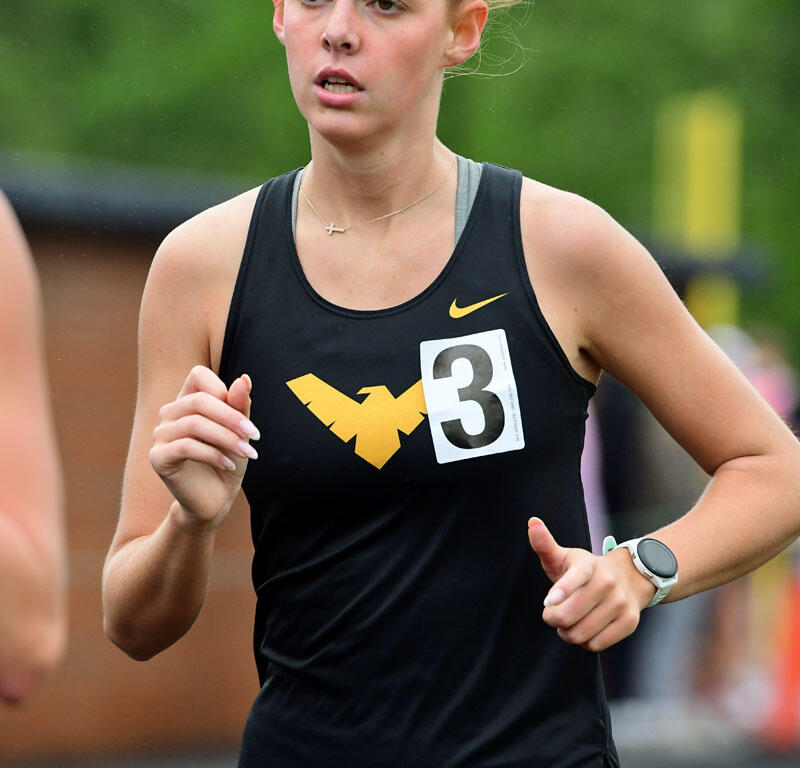 Female runner in a black sleeveless top with a bib number 3, mid-stride during a race, wearing a white smartwatch.
