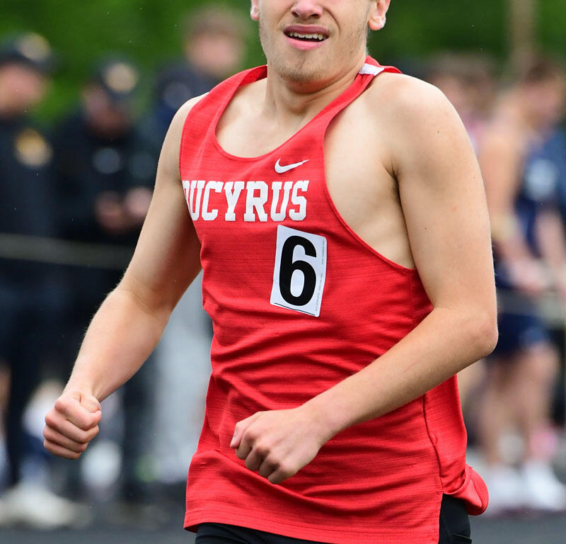 Male runner in a red singlet with race number 6, mid-stride on a track during a competition.