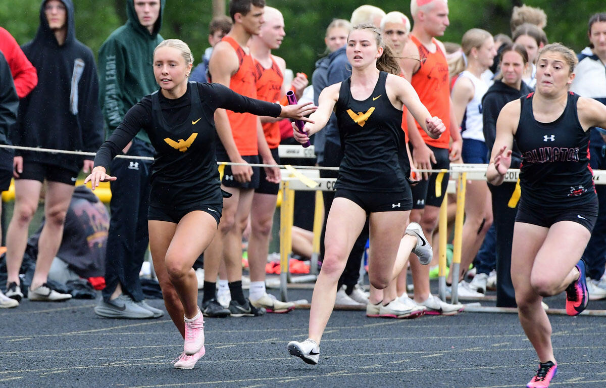 Girls' relay race: baton handoff between runners on a track with onlookers in the background