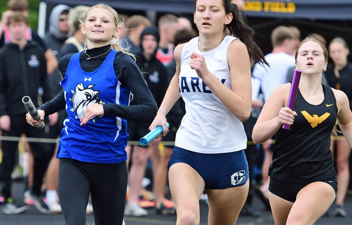 Three female track athletes sprinting in a relay race, each holding a baton as they run side by side.