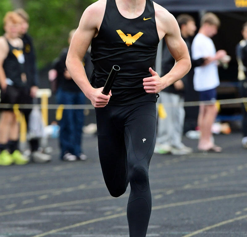 Male sprinter in black uniform with a yellow WV logo runs on a track, holding a baton during a relay race.