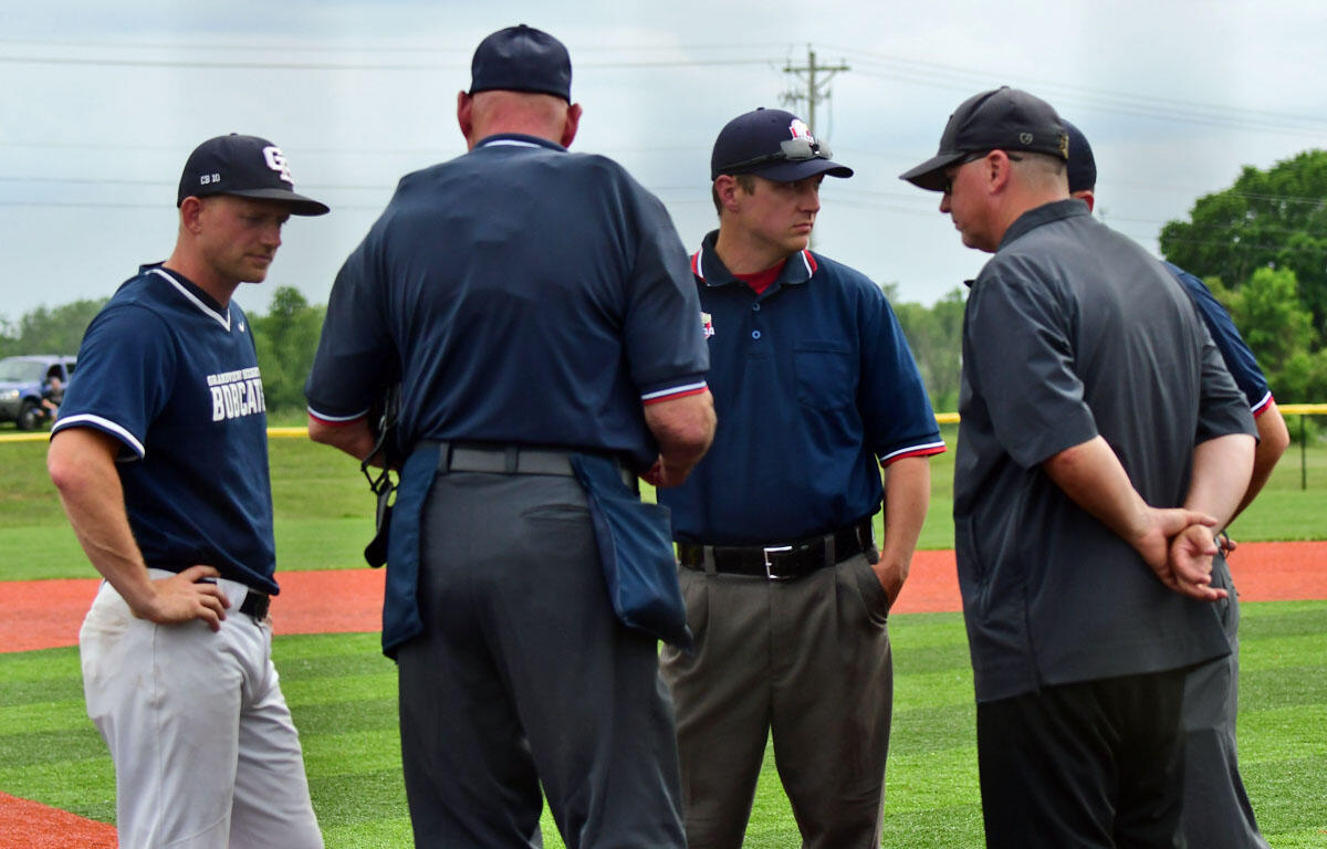 Group of baseball players and coaches in a circle, discussing strategy on a grassy field near the infield dirt.