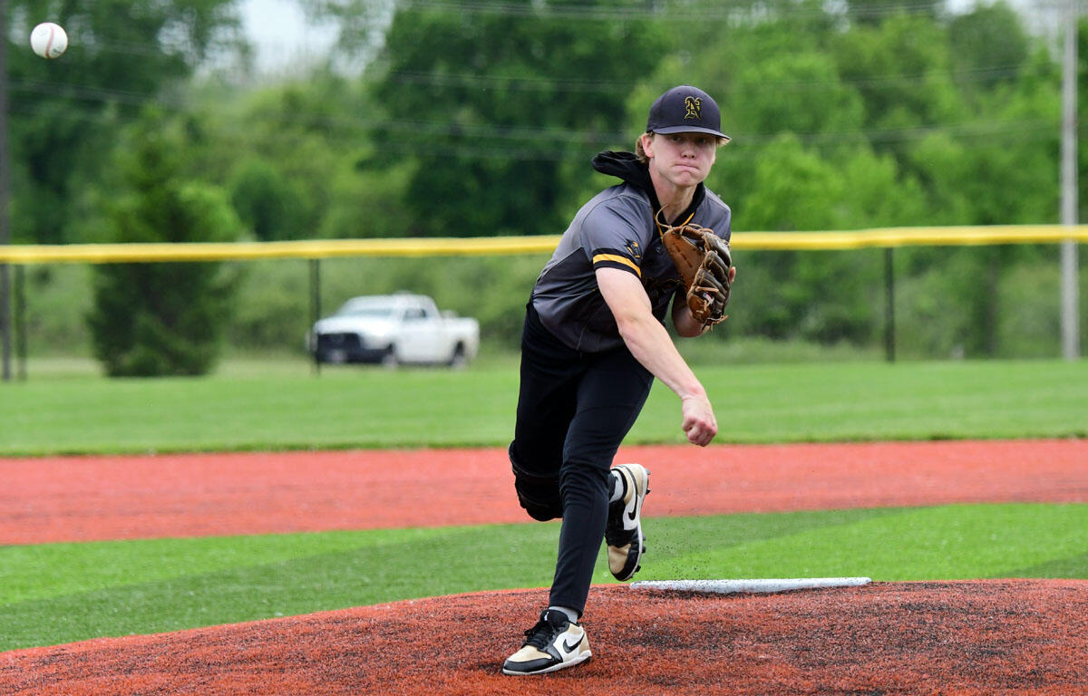 Baseball pitcher in gray and black uniform mid-pitch on the mound as the ball sails to the left.