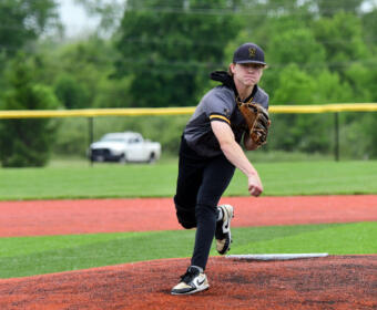 Baseball pitcher in gray and black uniform mid-pitch on the mound as the ball sails to the left.