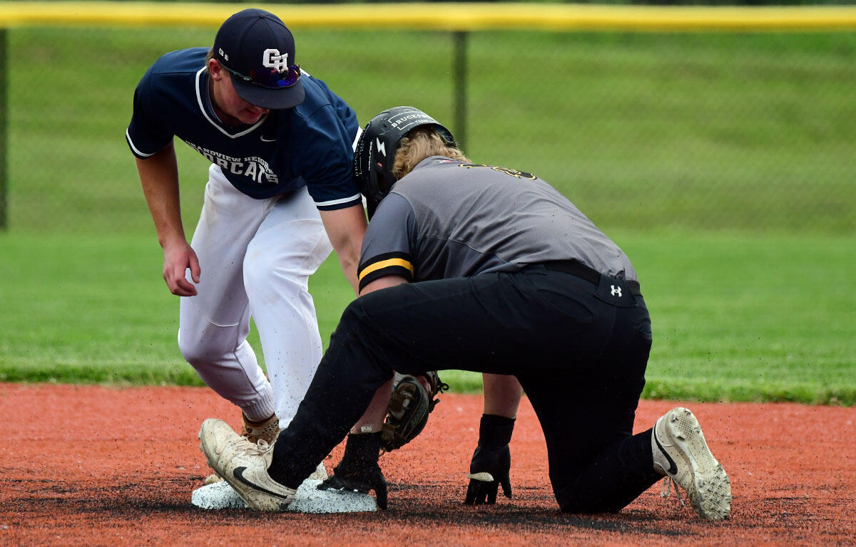 Two baseball players contest a bag on a dirt infield during a close play, one in a navy uniform and white pants, the other in gray and black kneeling by the base.