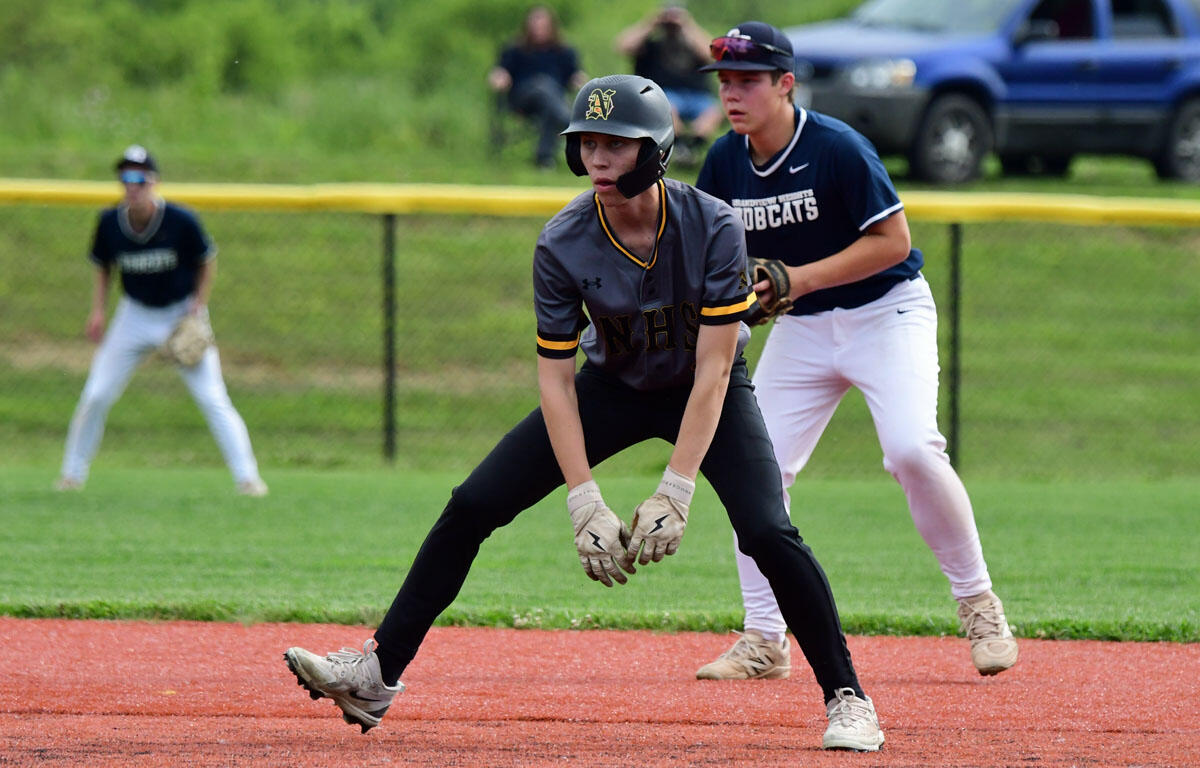 Youth baseball player in gray and black crouches to field a ground ball, gloves ready, on a red dirt infield with a teammate in navy awaiting behind him.
