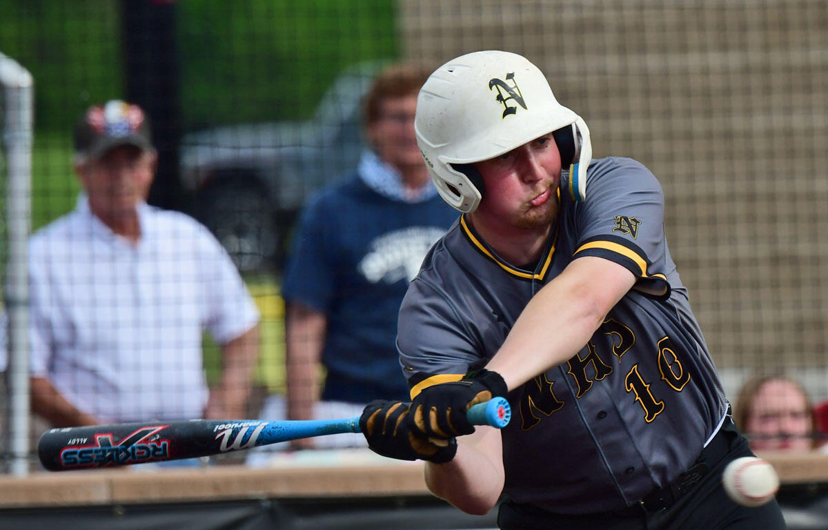 Baseball batter in gray and gold swings at a pitched ball during a game, helmet on, spectators behind.