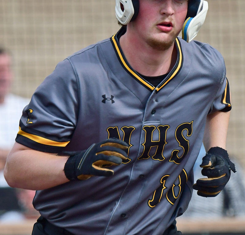 Baseball player in a gray WHS uniform running on the field, white helmet with a black N logo and batting gloves.