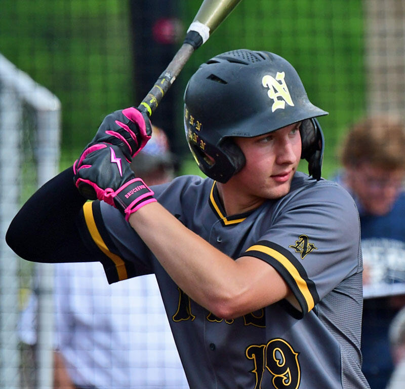 Baseball player in a gray uniform and black helmet swings a bat during a game, mid-swing with pink and black batting gloves nearby the plate.